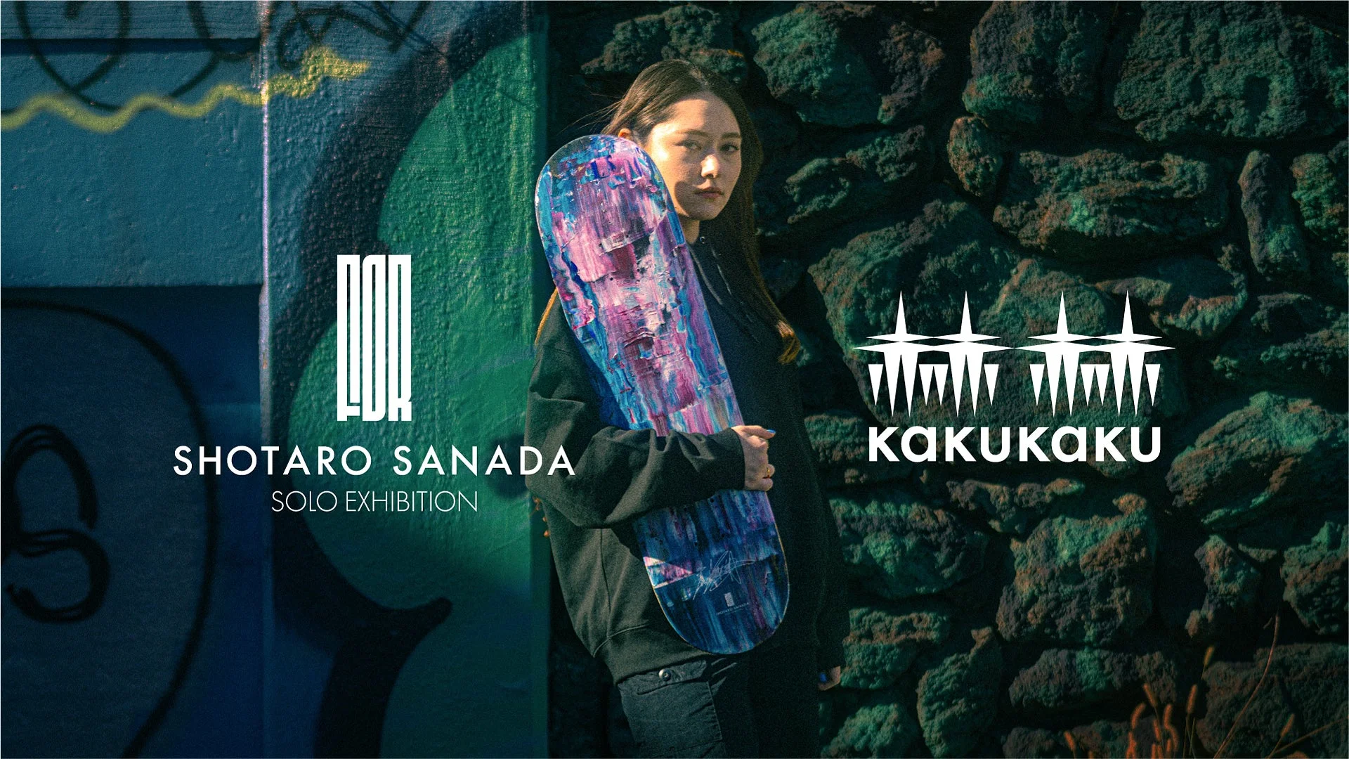 グラフィティが描かれた壁と石壁を背景に、カラフルなアートワークが施されたスケートボードを抱えた女性