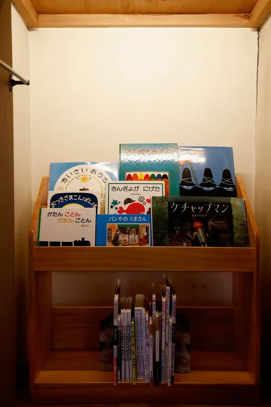 木製の棚に絵本や児童書が並べられた様子を写した写真です。上段には表紙が見えるように数冊の絵本が置かれており、下段には背表紙が見えるように多くの本が立てられています。