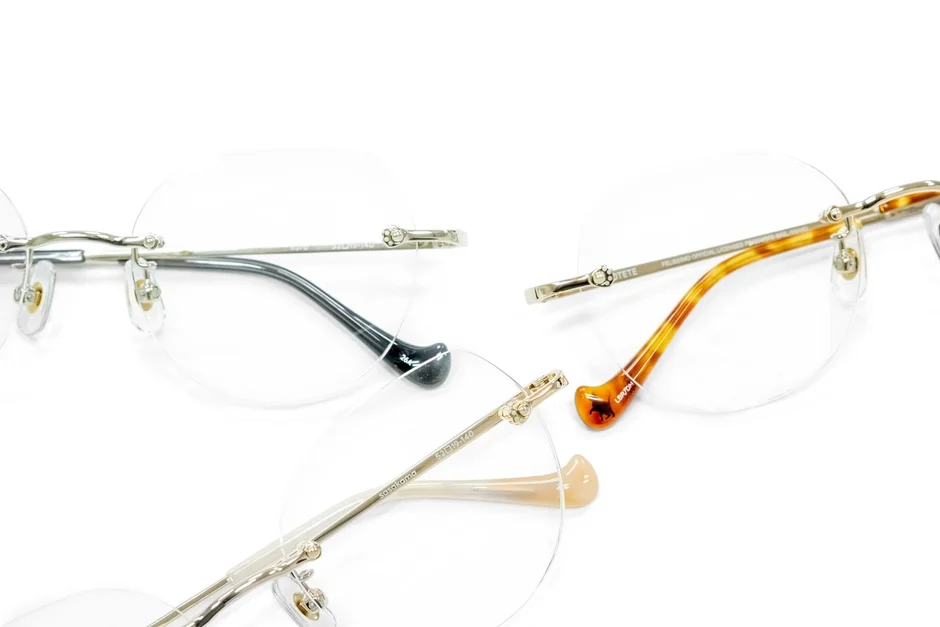 白い背景に、テンプルが異なる3種類のツーポイントメガネが並べられています。黒、べっ甲柄、ベージュのテンプルがあり、ブランド名や品番などの詳細が確認できます。メガネのデザインや質感が際立つ商品写真です。