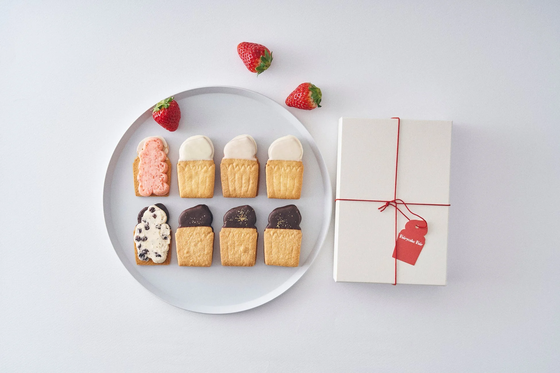 アイスクリームの形をした可愛らしいクッキーと、赤い紐で飾られたギフトボックス、そして新鮮なイチゴ