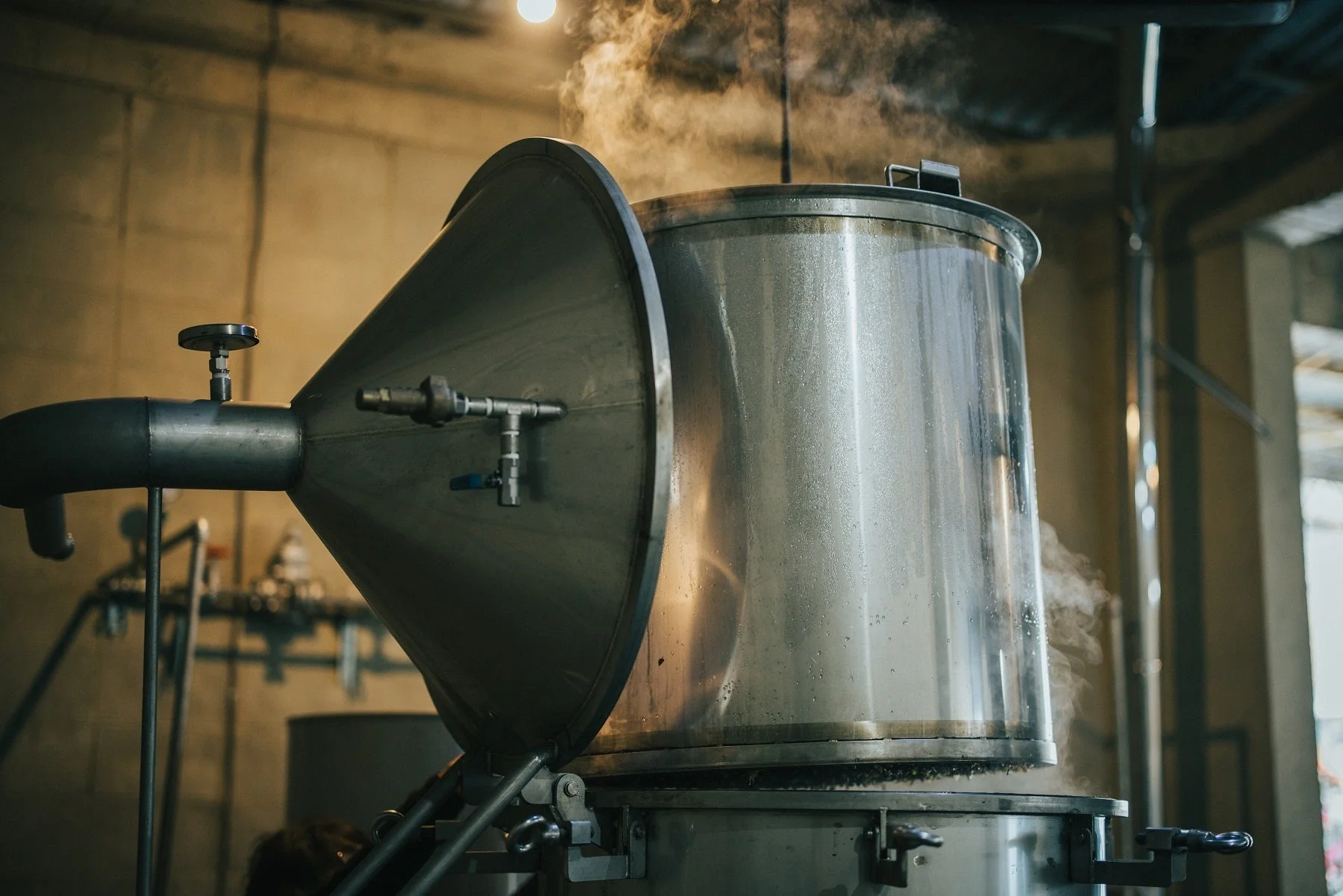 工場のような空間で大きなステンレス製タンクから立ち上る蒸気