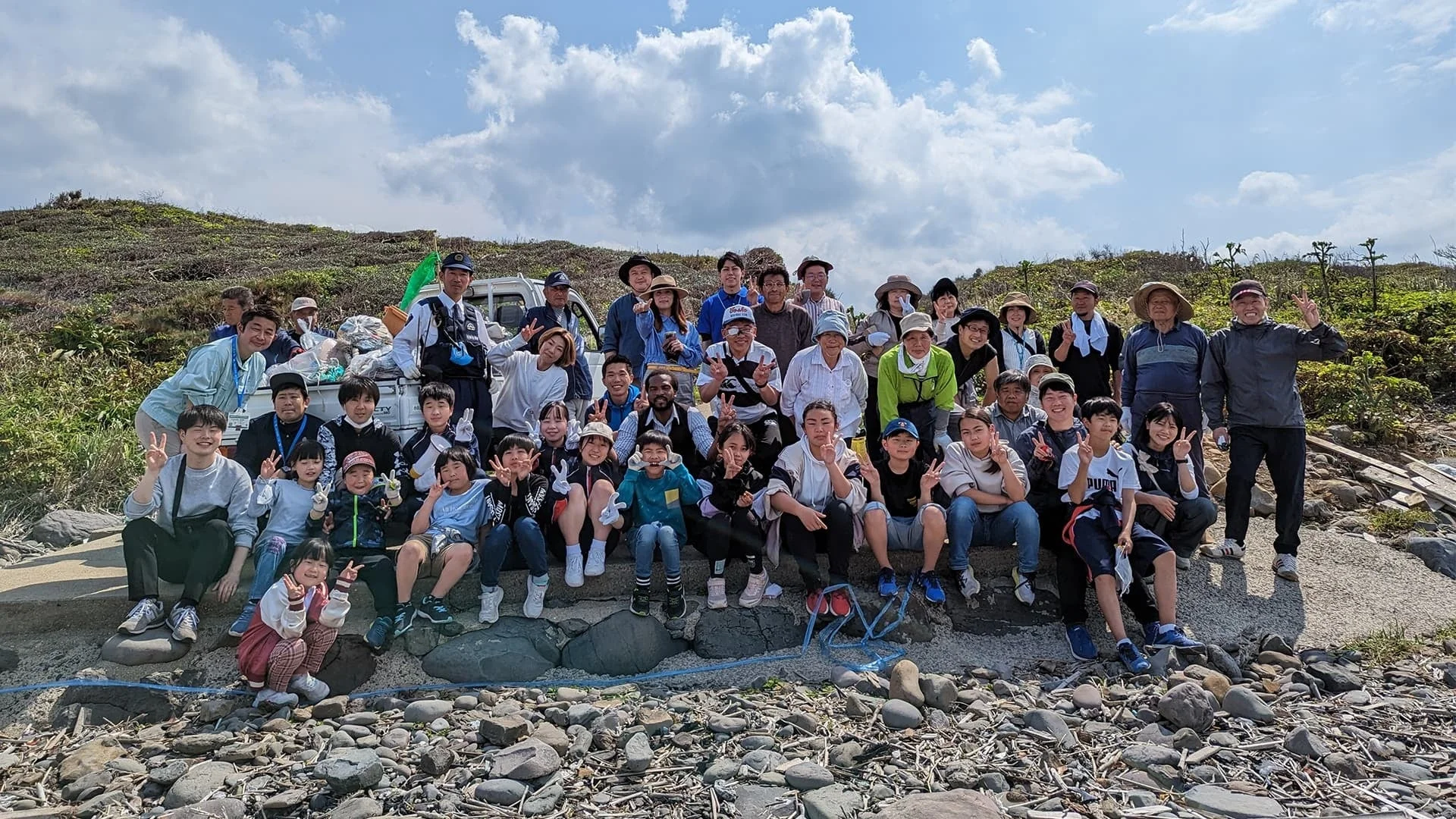 屋外でピースサインをする人々の集合写真