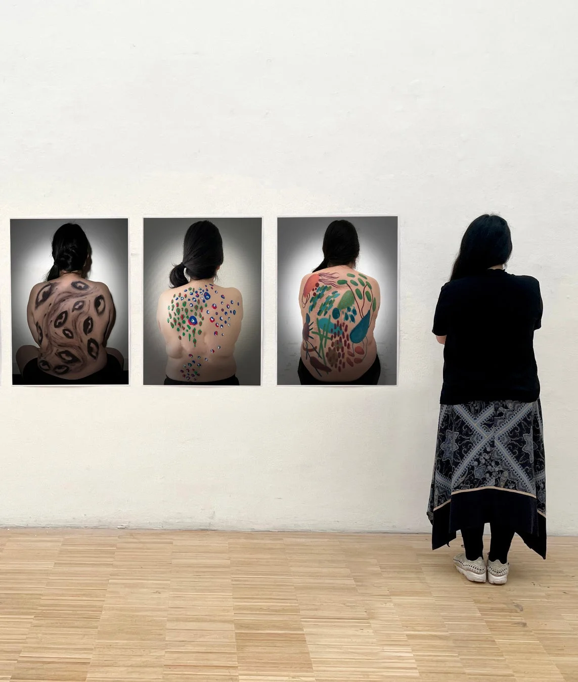 ギャラリーで、一人の人物が壁に展示された三つのアート作品を鑑賞しています。