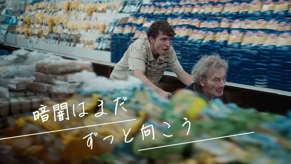 スーパーマーケットのシーンと日本語テキスト「暗闇はまだずっと向こう」