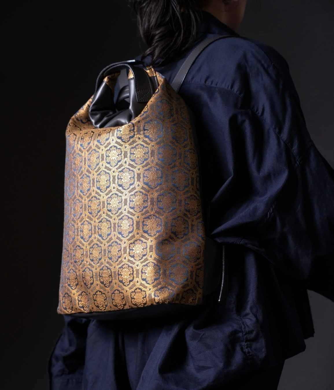 紺色の衣服を身につけた人物が、金色と紺色の伝統的な六角形模様のリュックサックを背負っている様子