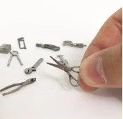 指でつまんだ極小のハサミと、その周りに散らばる様々なミニチュア工具