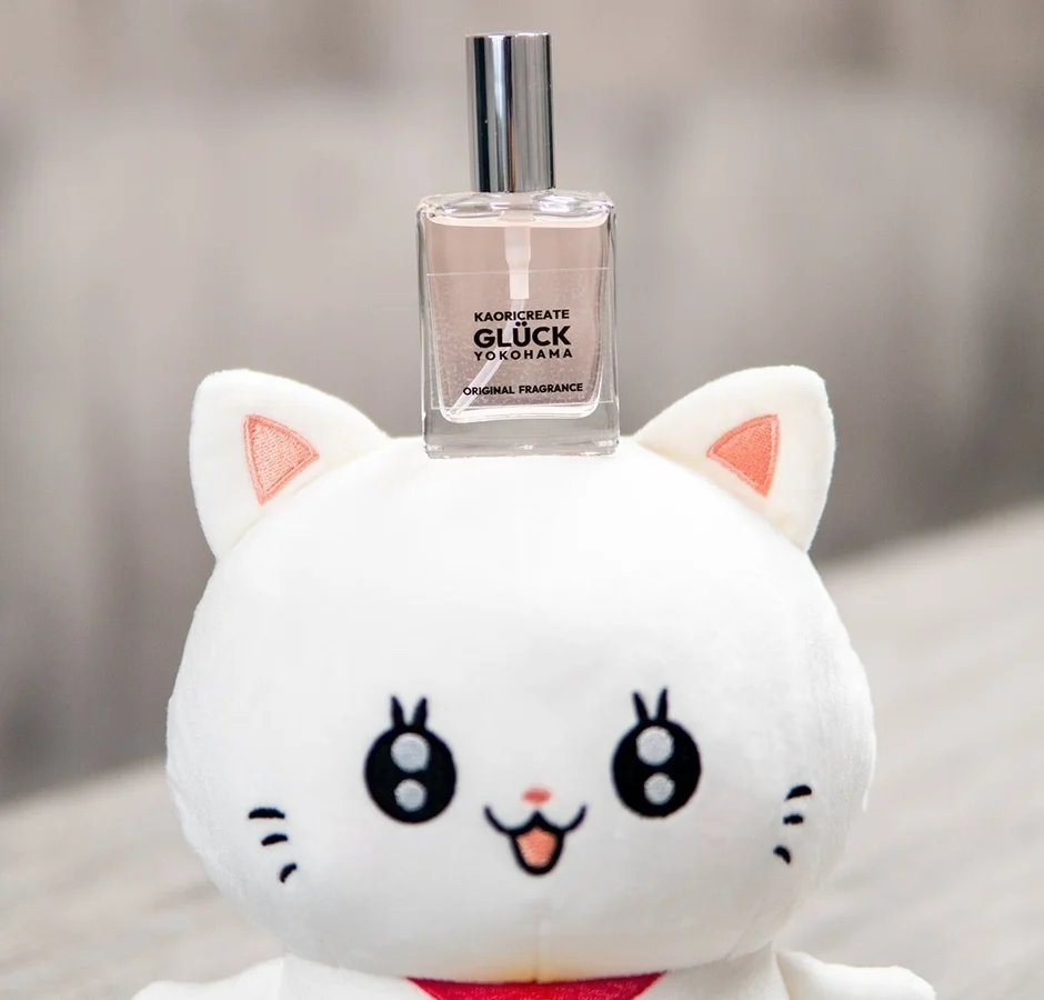 白い猫のぬいぐるみの頭の上に、ピンク色の液体が入った香水ボトルが置かれています。