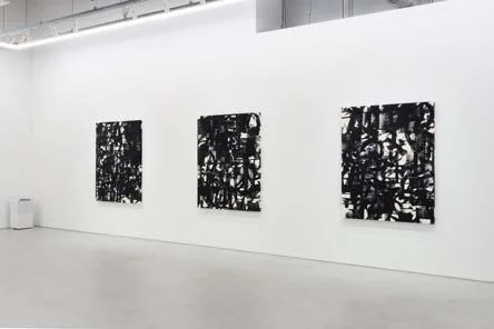 白い壁の現代的なアートギャラリーに、黒と白の抽象画が3点展示されている