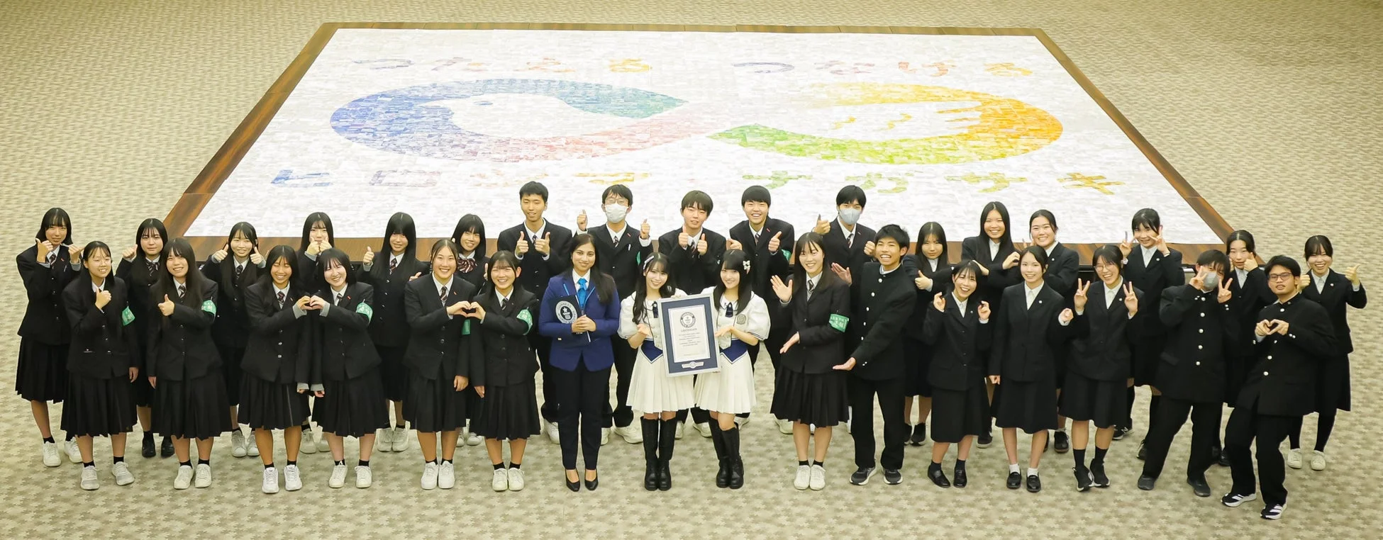 モザイクアートの前で認定証を持つ学生たち