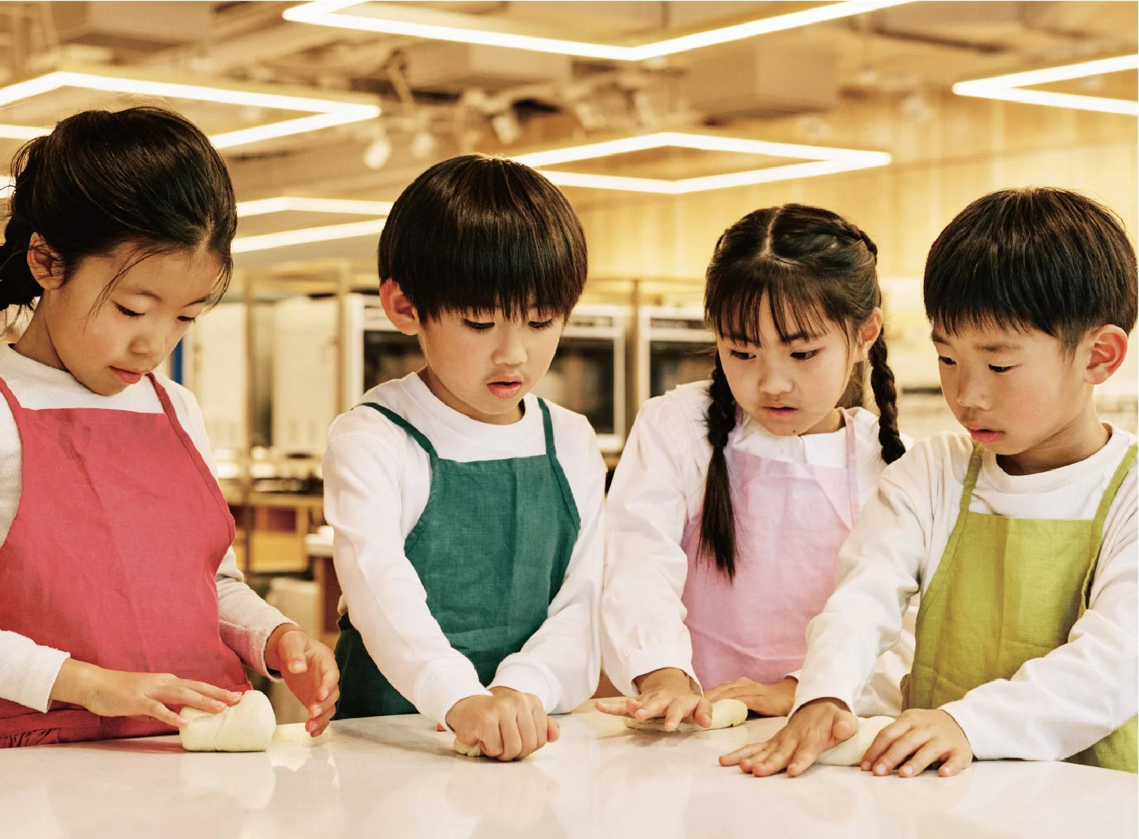 子供たちがエプロンを着てパン生地をこねている様子