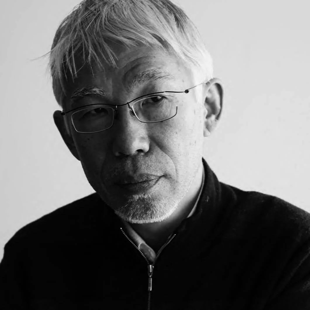 白髪と顎髭の男性が眼鏡をかけ、カメラをまっすぐ見つめているモノクロのポートレート