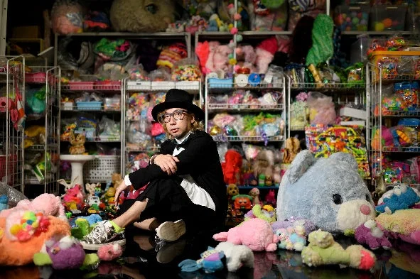 黒いハットとスーツを着用し、作品に囲まれて座る増田セバスチャン氏