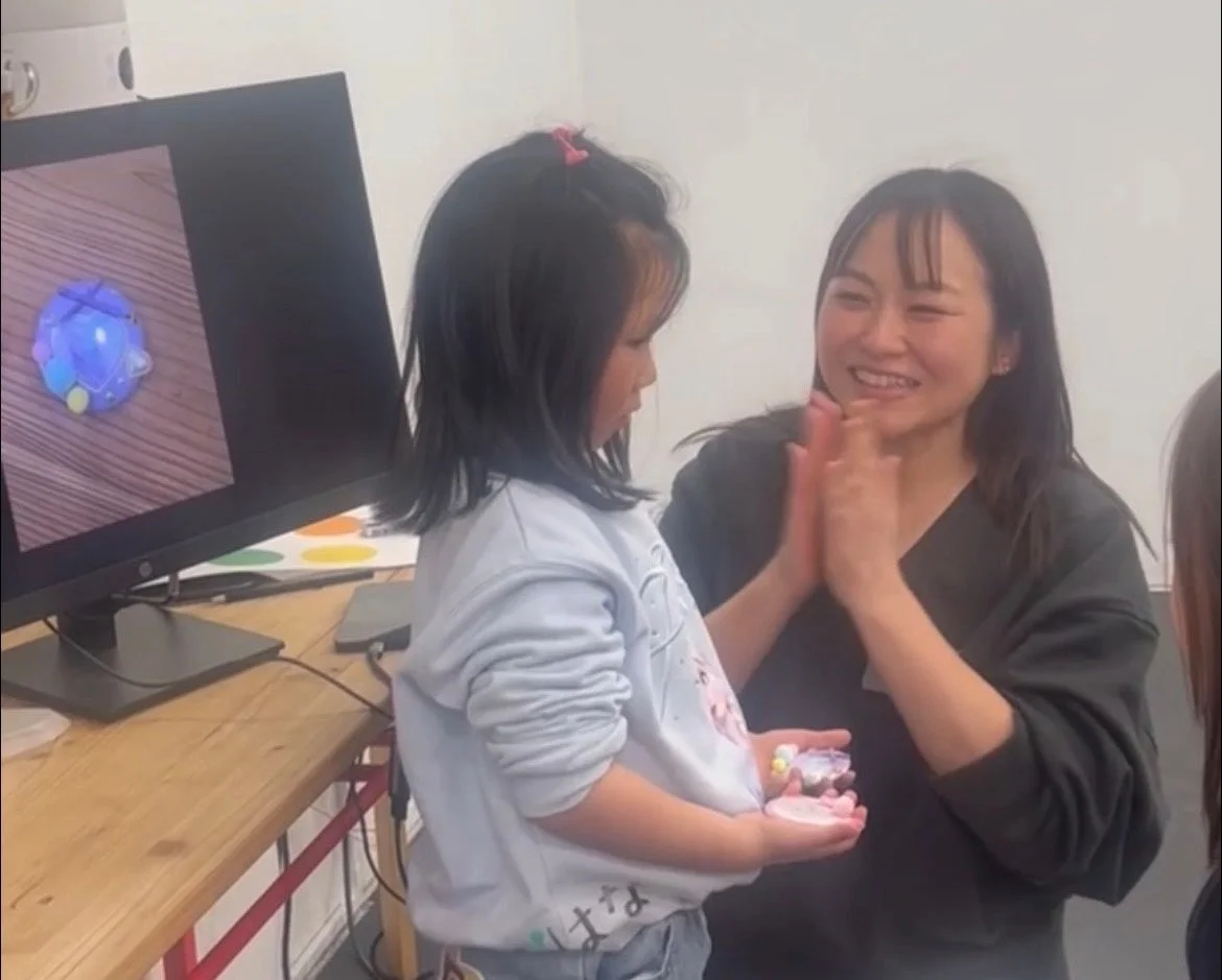 モニターに集中する子供と拍手する女性