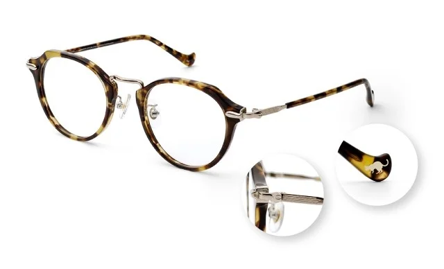 べっ甲柄の丸いフレームが特徴的なメガネの製品写真です。テンプルには金属製の装飾が施され、耳にかける部分には猫のロゴがあしらわれています。全体的にクラシックでおしゃれな印象を与えます。