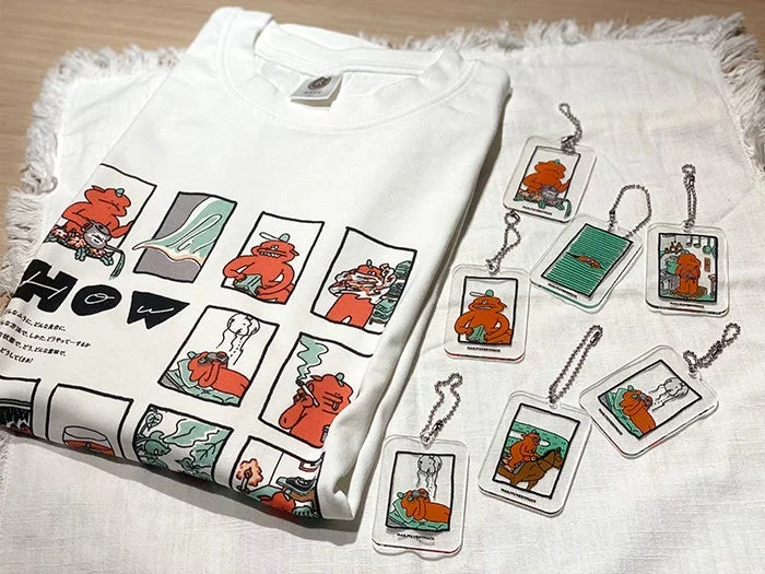 白いTシャツと、それに描かれたオレンジ色のコミック風キャラクターのイラストをモチーフにしたアクリルキーホルダー