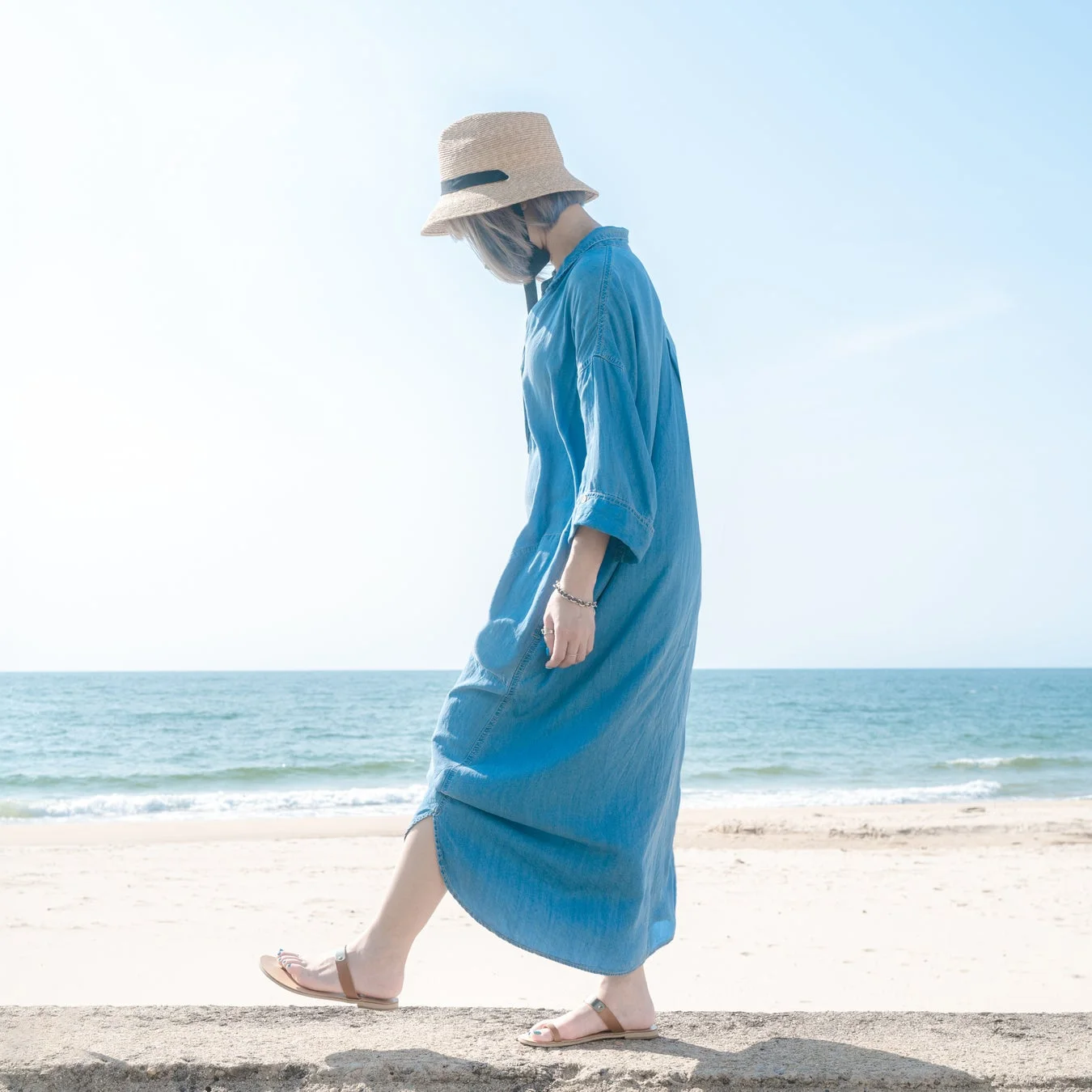 青いデニムワンピースの女性がビーチを歩く様子