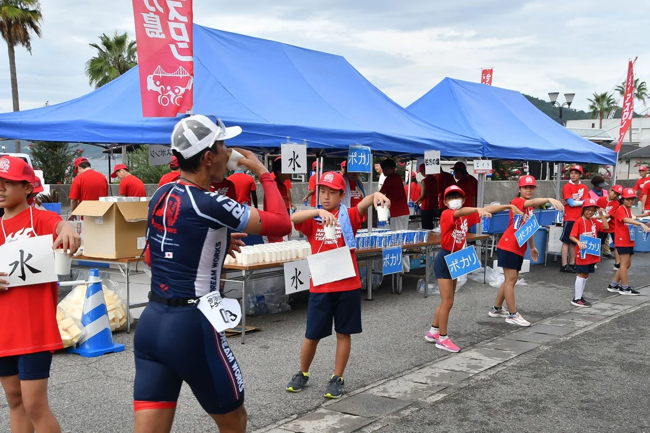 トライアスロン大会のエイドステーションで、参加者が水分補給をしています
