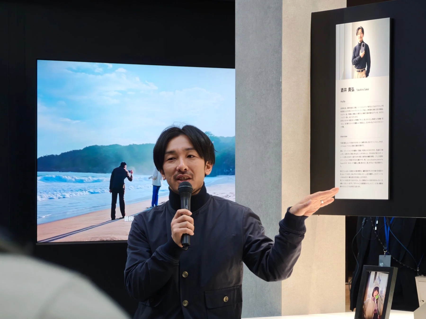 一人の男性がマイクを持ってプレゼンテーションを行っているイベント風景