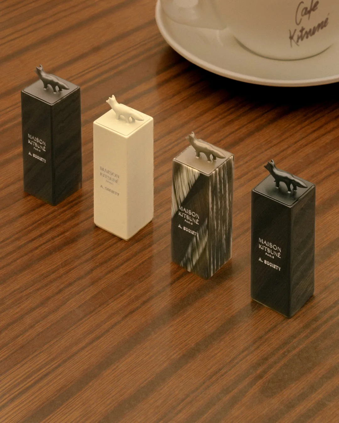 木製のテーブルの上に、キツネのフィギュアが乗った「MAISON KITSUNE」の長方形のオブジェクトが4つ並べられている