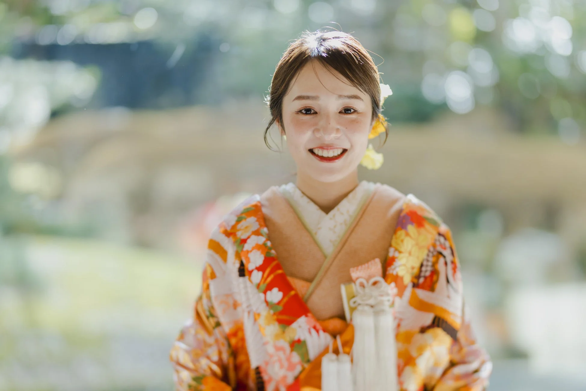 華やかな着物を身につけた若い女性が、にこやかにカメラを見つめています。明るい笑顔が印象的で、伝統的な和装の美しさが際立っています。