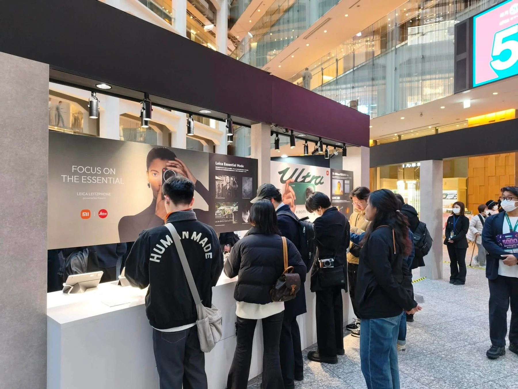 ショッピングモールのような広々とした空間で、LeicaとXiaomiのコラボレーション製品の展示ブースに多くの人々が集まっている様子