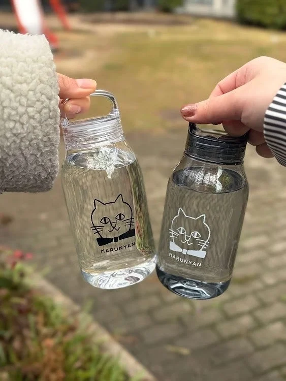 2人の人物が猫のキャラクター「MARUNYAN」が描かれた透明なドリンクボトルを手に持っている画像です。ボトルの中には水が入っており、屋外で楽しんでいる様子が伺えます。
