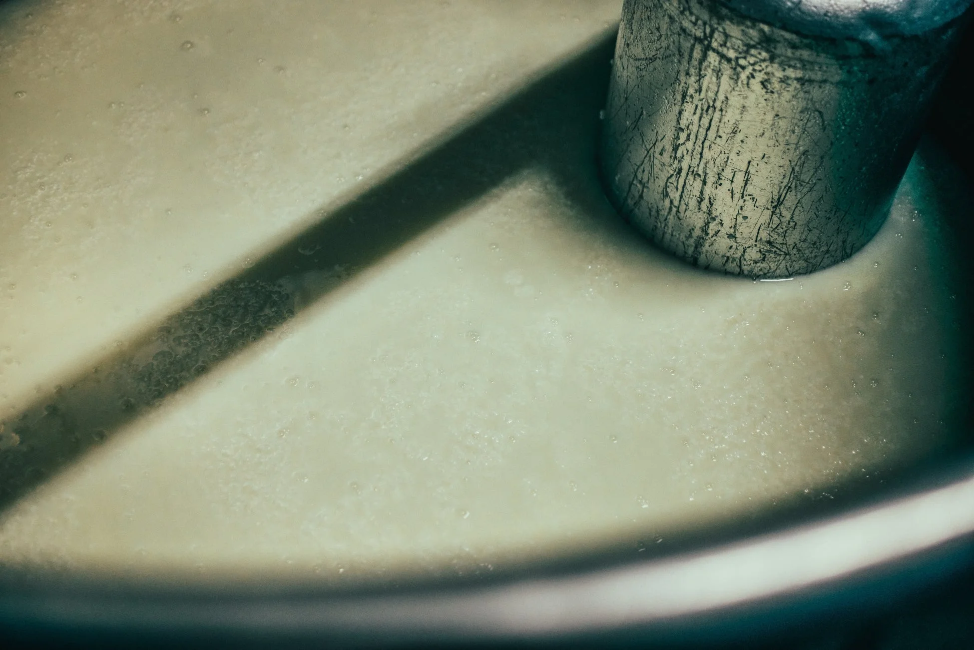 淡い色の液体に金属製の円筒が浸かっており、多数の泡が見られる