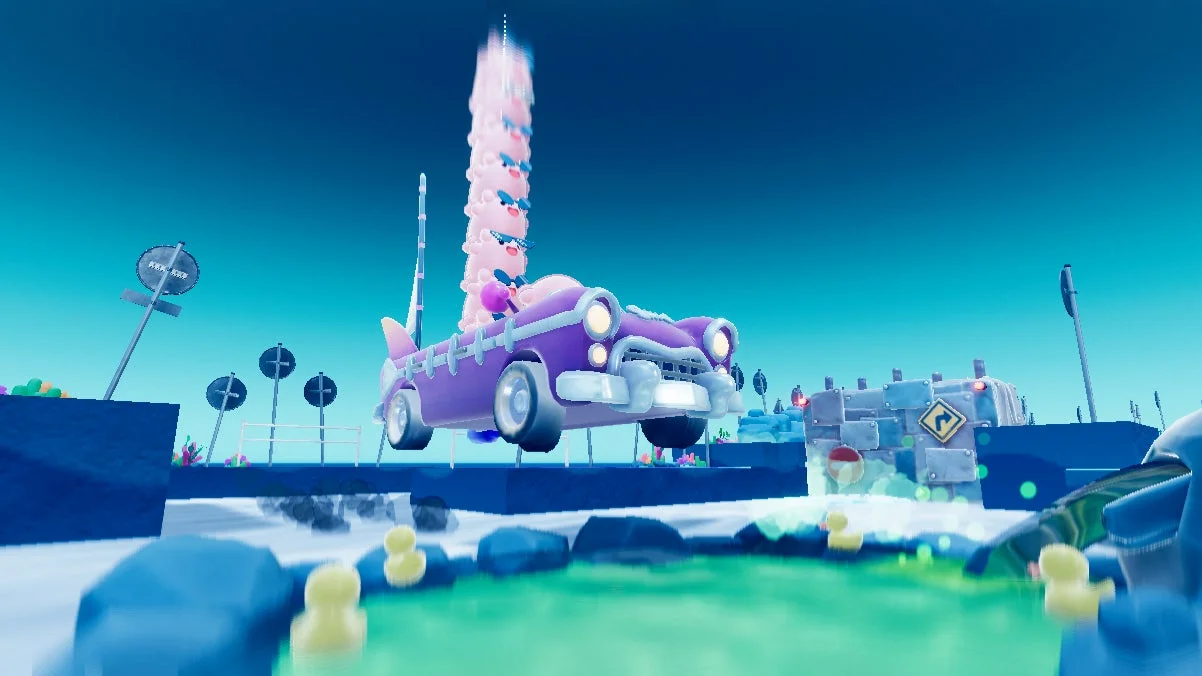 明るい青空の下、ピンクのキャラクターが積み重なって乗った紫色のクラシックカーが浮遊しています。下には緑色の水とゴム製のアヒル、そして複数の標識が見える、ファンタジーのようなゲームの世界の一場面です。