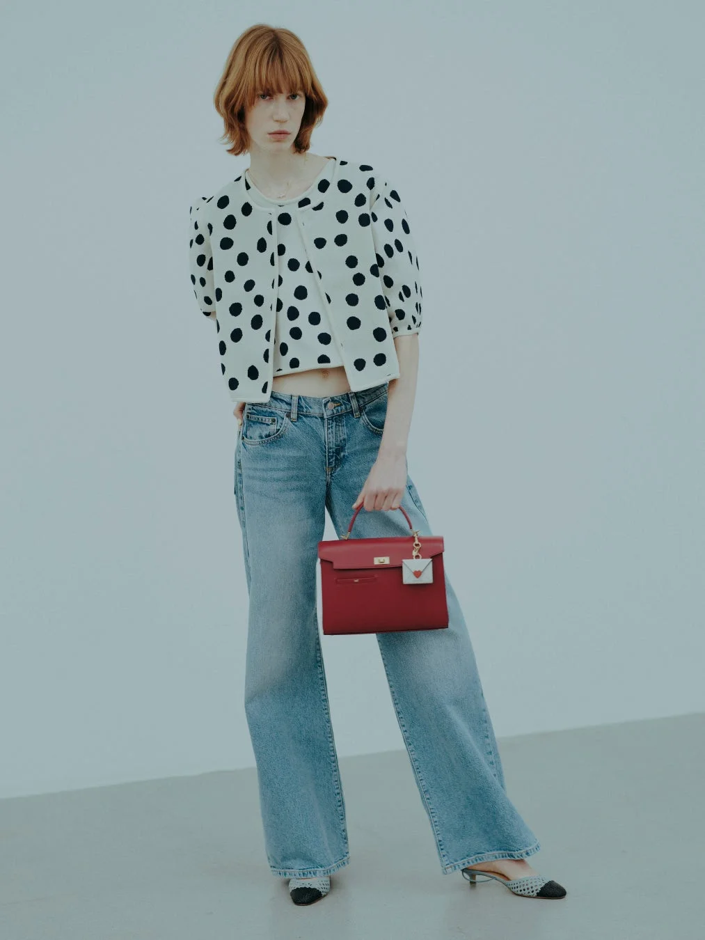 水玉模様のクロップドカーディガンとワイドジーンズを着用し、赤いハンドバッグを持った女性モデルの全身像