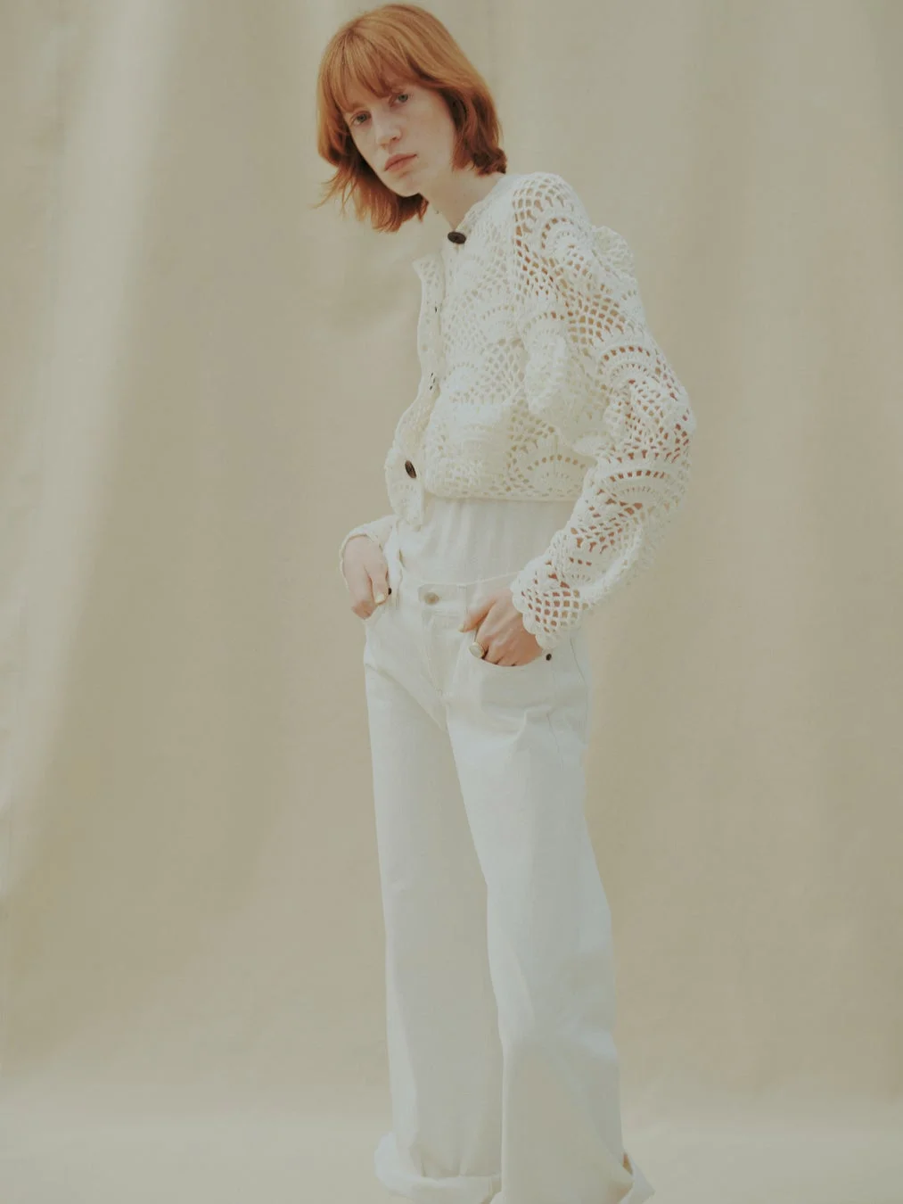 白いクロシェニットのカーディガンと白いワイドパンツを着用した女性のポートレート