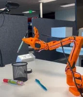 オフィスデスクでペンを操作するオレンジ色のロボットアーム