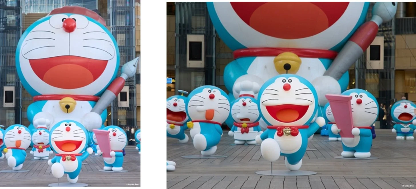 巨大なドラえもんのバルーンを中心に、様々なポーズや衣装のドラえもんフィギュアが屋外の広場に展示されている様子