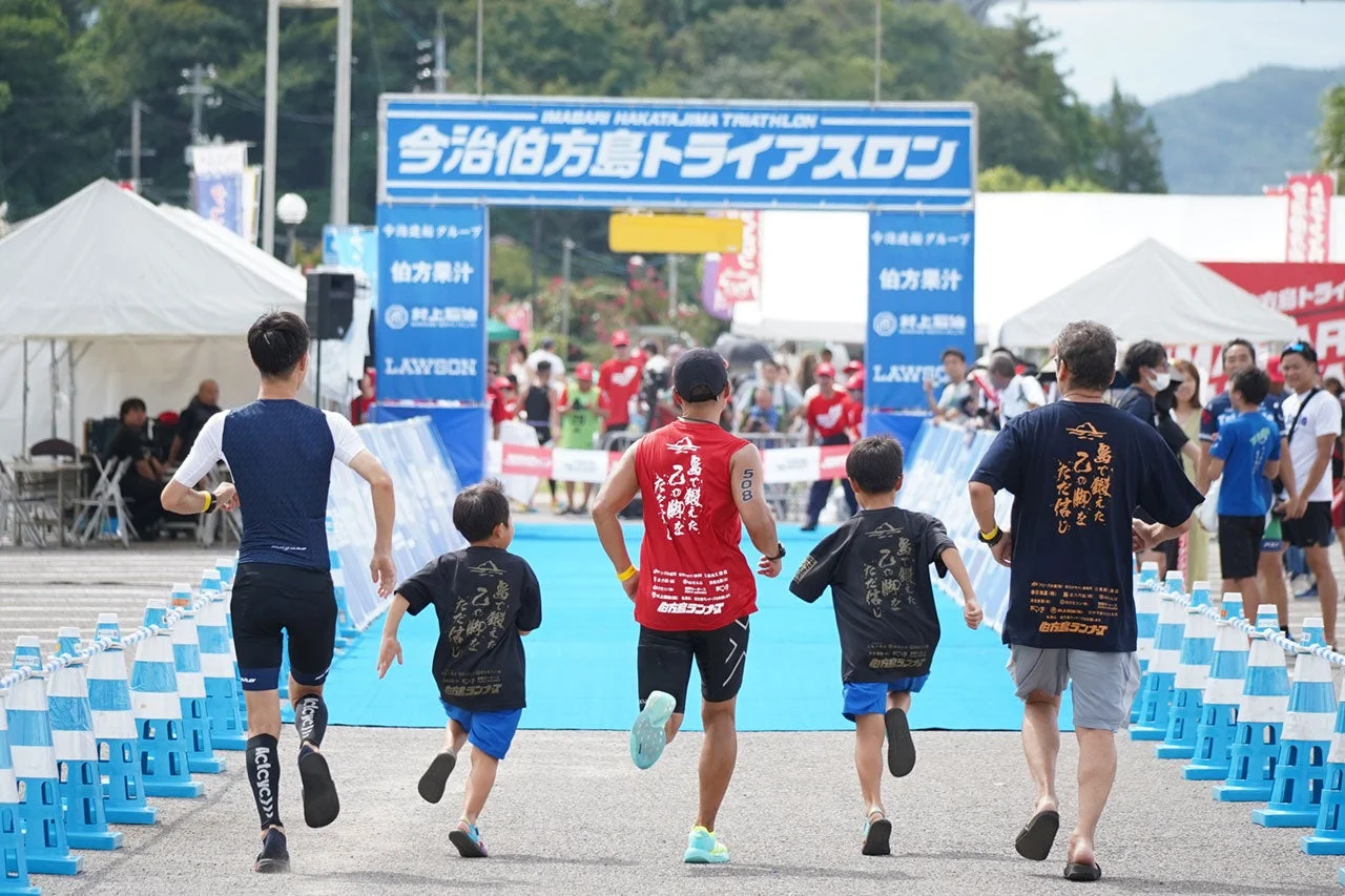 今治伯方島トライアスロンのゴールゲートに向かって、大人と子供が一緒に走る参加者たちの様子