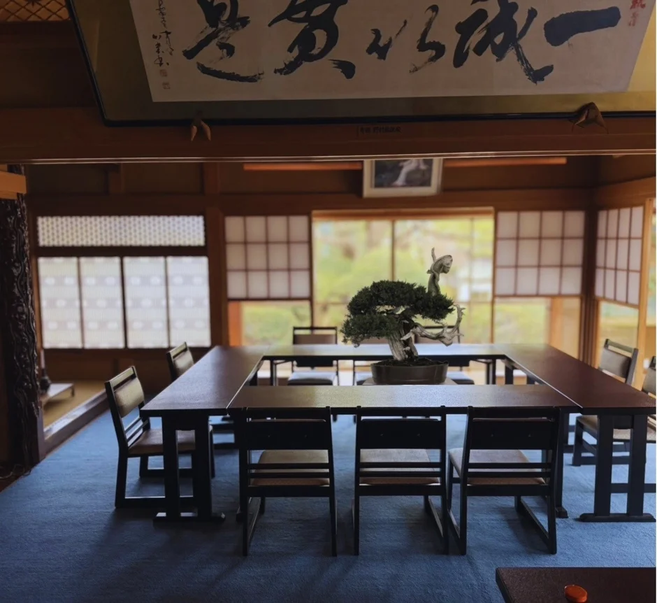 伝統的な日本家屋の和室で、盆栽が置かれた木製のテーブルと椅子が配置されています。