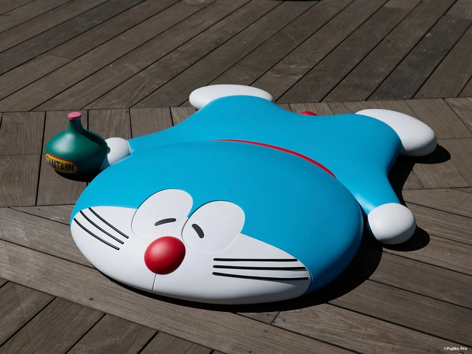 木のデッキに横たわる大きなドラえもんのフィギュア