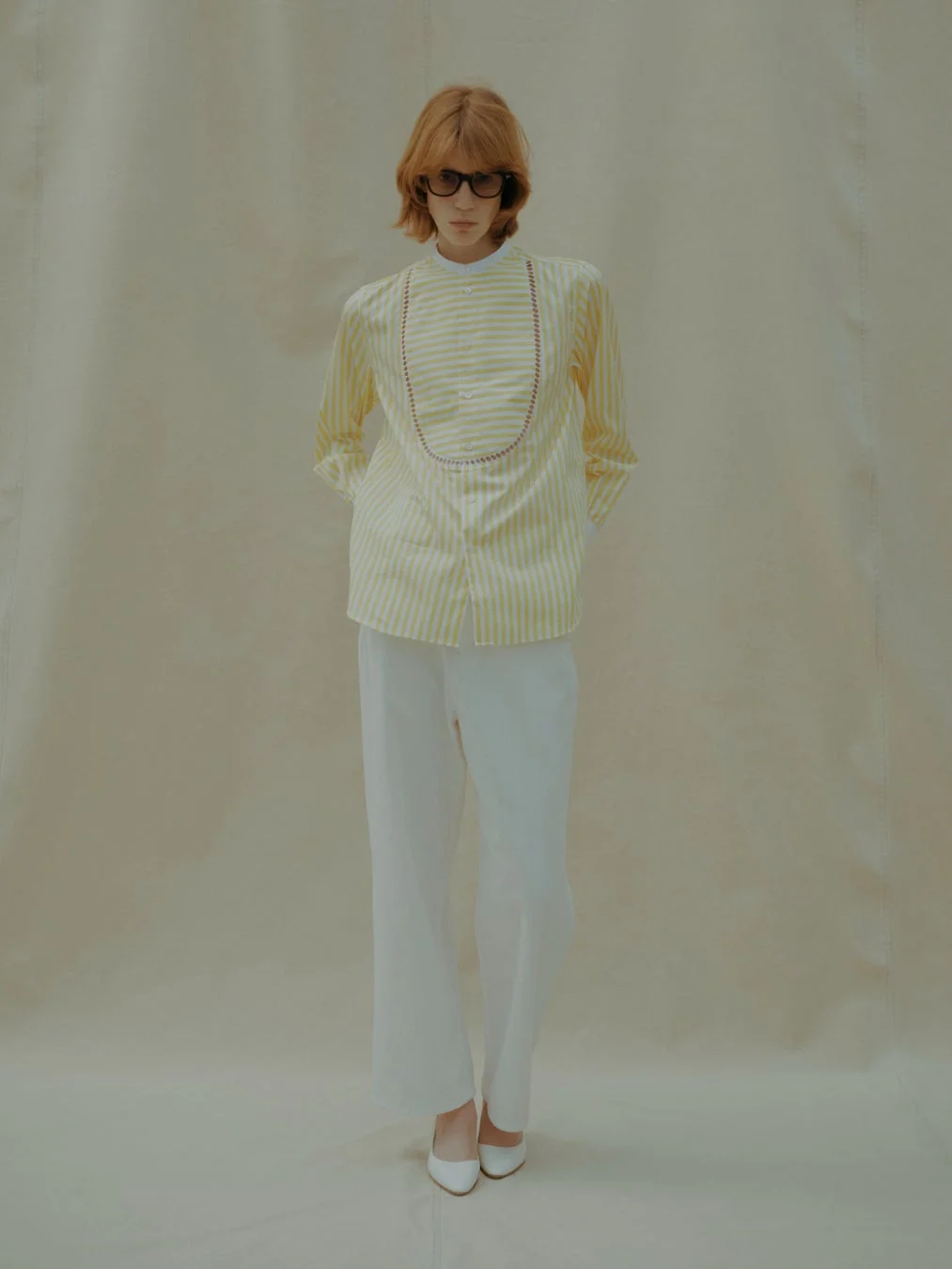 黄色と白のストライプシャツに白いワイドパンツ、白いパンプスを合わせた女性モデル