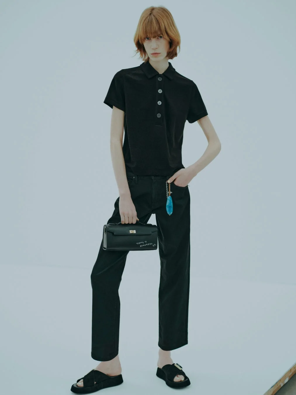 黒いポロシャツとパンツ、厚底サンダルを着用したショートヘアのモデル