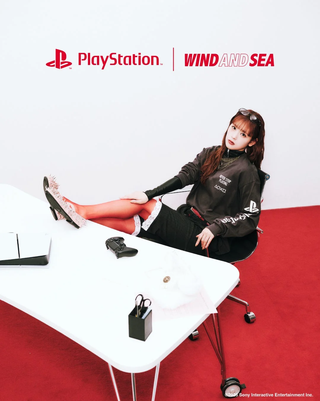 PlayStationとWIND AND SEAのコラボレーションを示す画像。赤いタイツとPlayStationロゴ入りスウェットを着用した女性が、白いテーブルに置かれたPlayStation 5とコントローラーの傍らで椅子に座っている。赤と白を基調としたスタイリッシュな一枚。