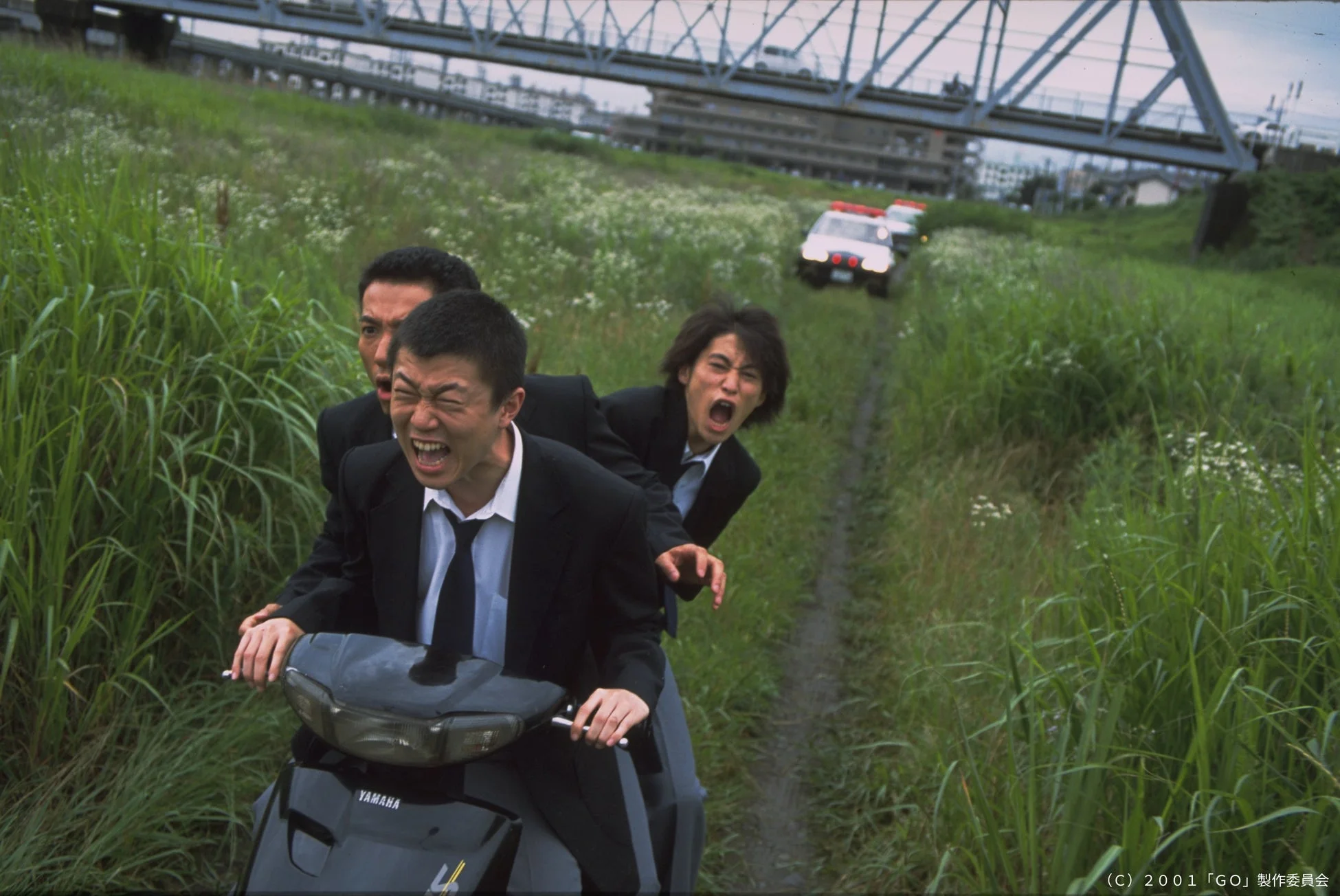 スクーターで疾走する男性たちとパトカー