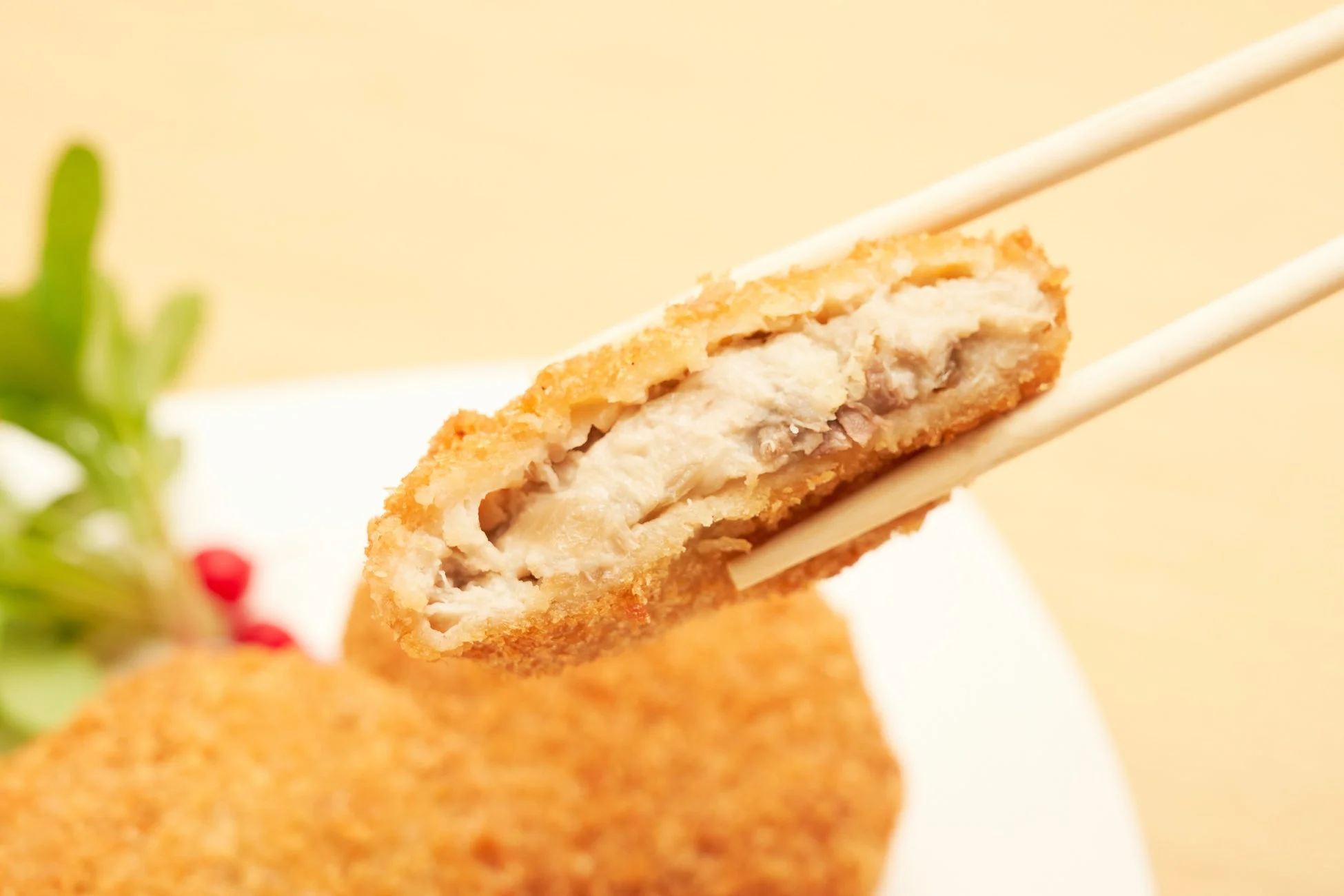 揚げたてのサクサクとした衣のコロッケかメンチカツを箸で持ち上げた瞬間を捉えた画像です。