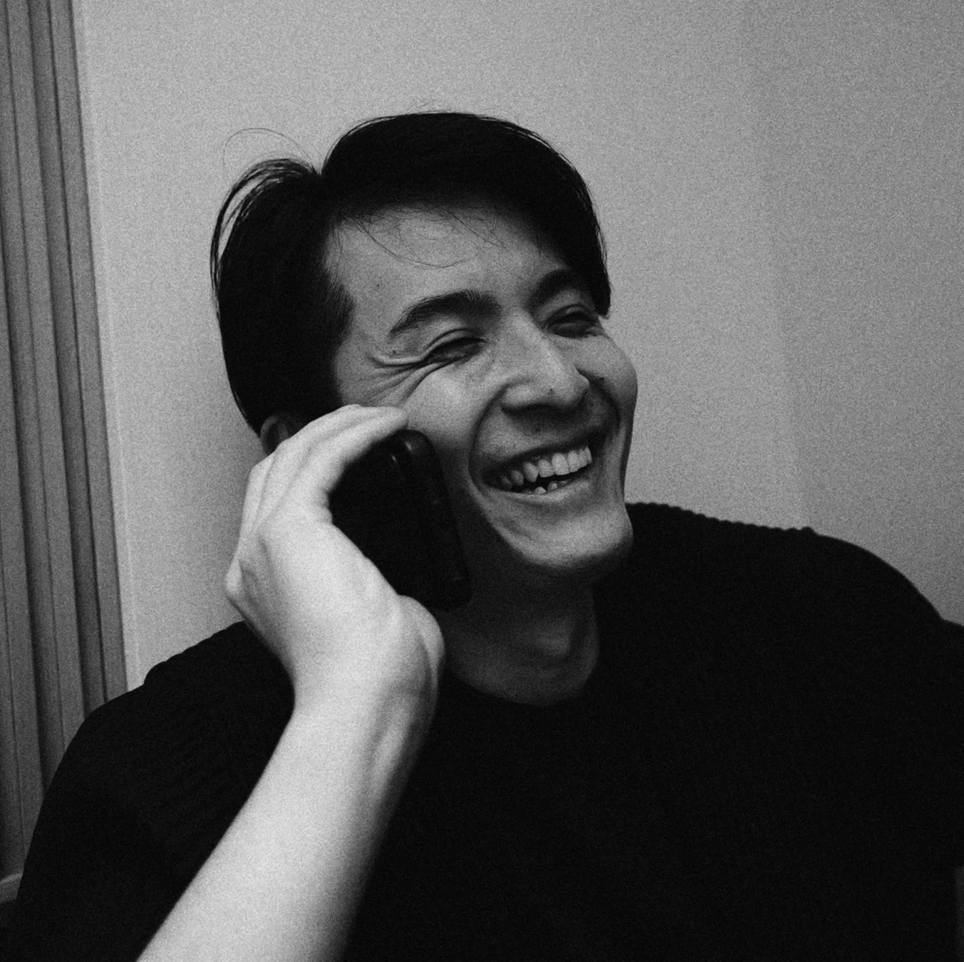 白黒写真で、スマートフォンで話しながら大笑いしている男性の姿。