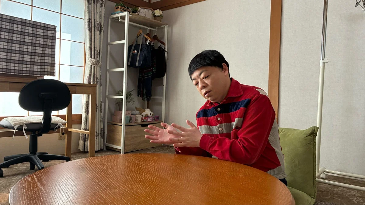 赤いストライプのシャツを着て、身振り手振りを交えながら話す男性