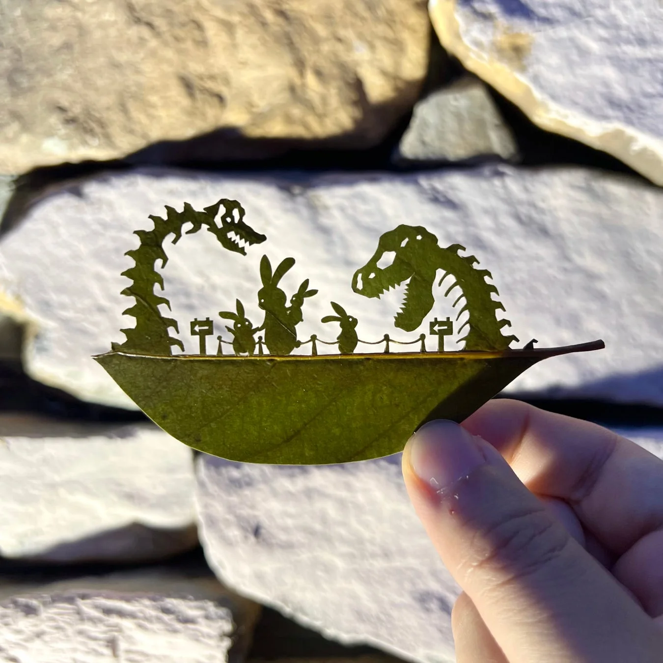 一枚の葉っぱに恐竜の骨格とウサギたちが繊細に切り抜かれたアート作品です。ウサギたちが恐竜の骨格を見上げているような、物語性のあるユニークな情景が表現されています。