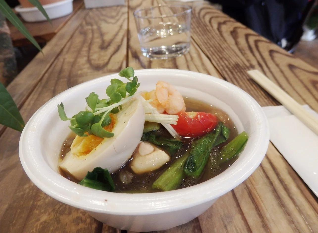 木製のテーブルに置かれた、卵、エビ、ミニトマト、野菜が盛り付けられた温かいスープ料理です。