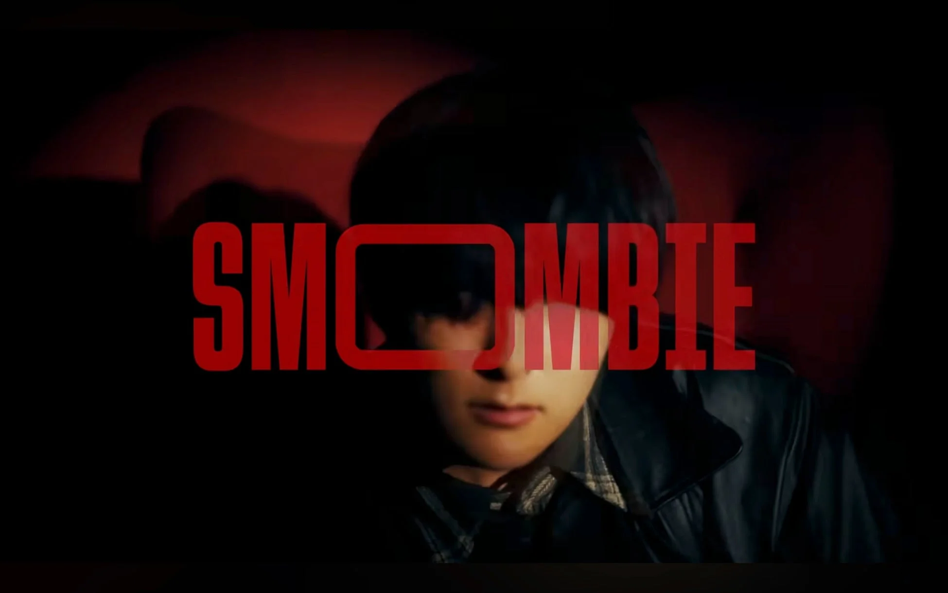 暗闇の中、赤文字で「SMOMBIE」と書かれたタイトルロゴが、顔の一部を隠すように配置された若者の顔を捉えています。映画のポスターやタイトル画面のような雰囲気で、スマートフォンに没頭する現代人を風刺するようなテーマを感じさせます。