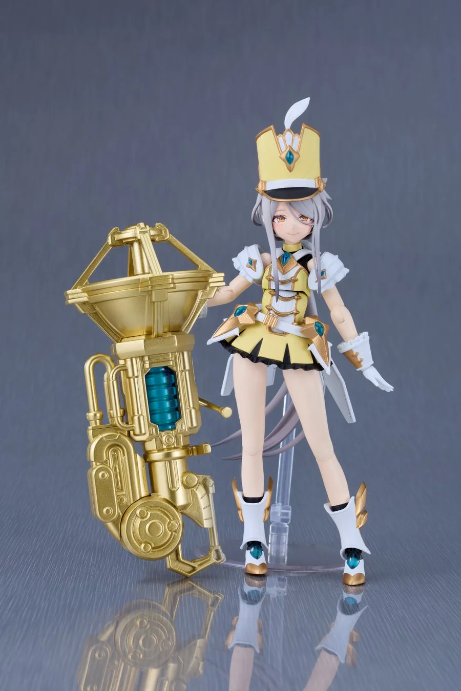 黄色と白の華やかなバンド衣装をまとった美少女フィギュアが、精巧な金色の楽器のようなメカの隣に立っています。