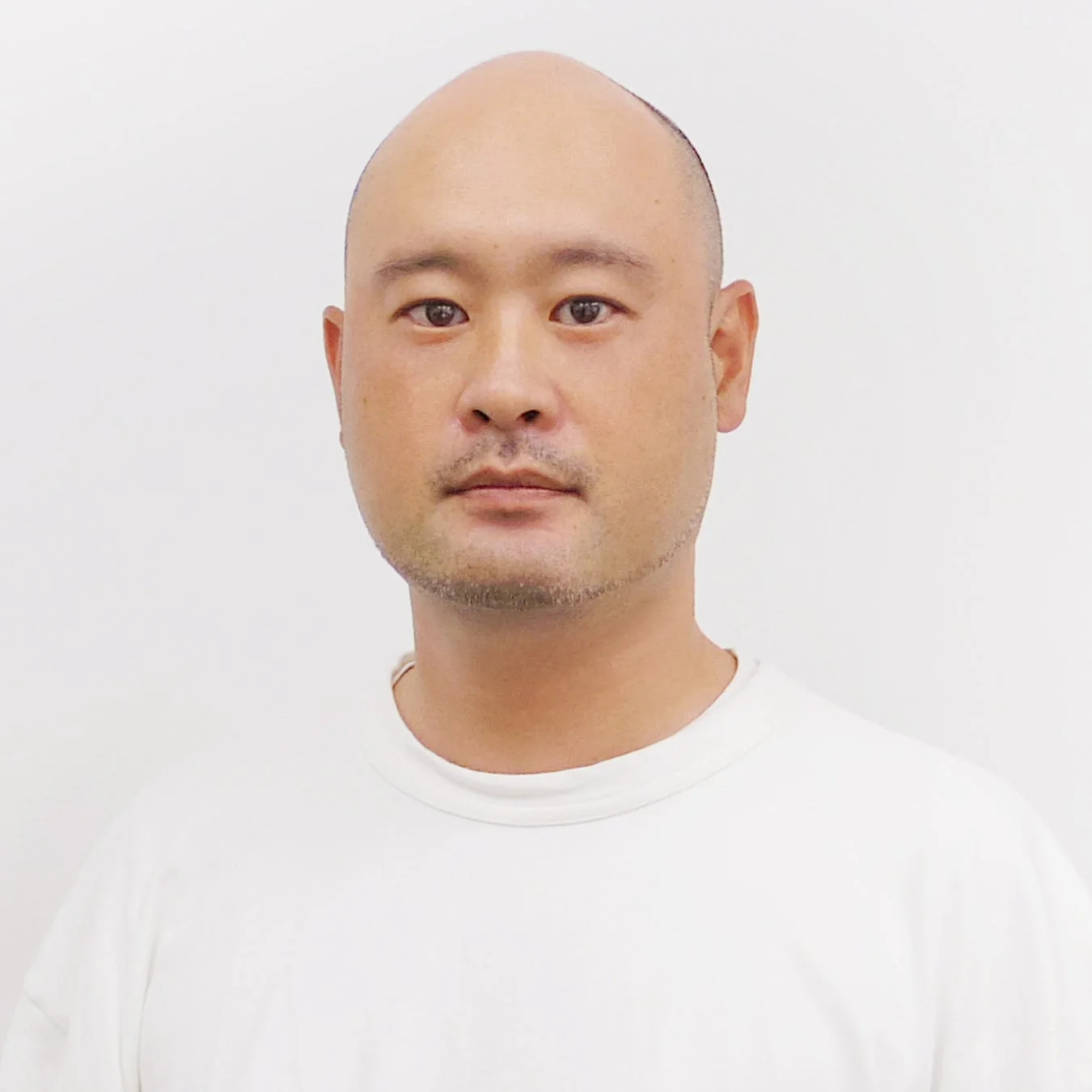 白いTシャツを着た坊主頭の男性のポートレート。
