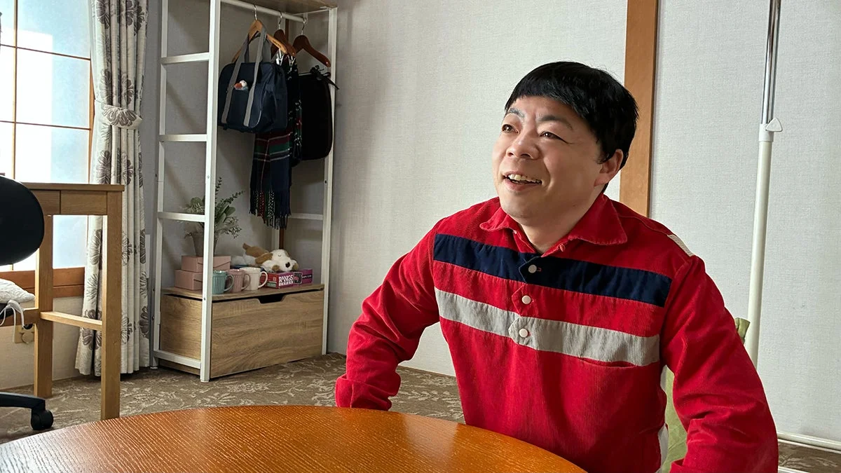 木製のテーブルに座り、笑顔で遠くを見つめる男性