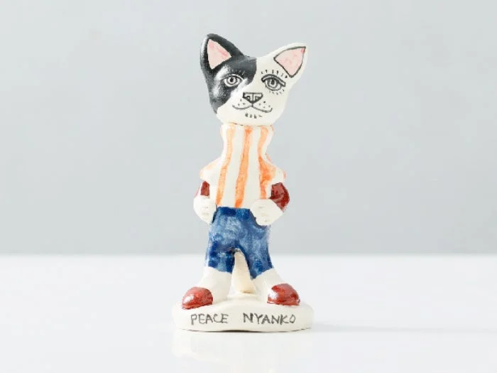 白黒の顔にオレンジと白のストライプシャツ、青いズボンを履いた猫のようなキャラクターの置物