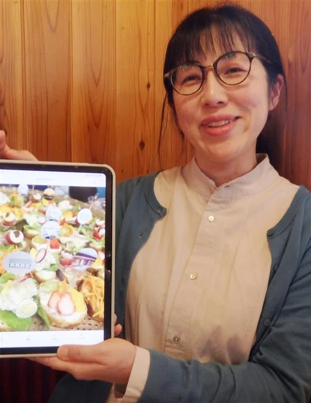 笑顔の女性がタブレットを手に持ち、画面には色とりどりの小さな料理が並んでいます。